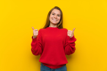 Young woman over yellow wall with thumbs up gesture and smiling