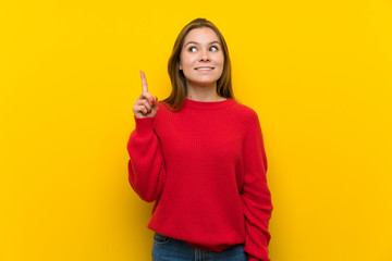 Young woman over yellow wall intending to realizes the solution while lifting a finger up