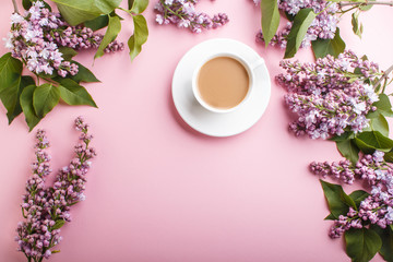 Purple lilac flowers and a cup of coffee on pastel pink background.