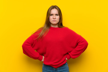 Young woman over yellow wall angry