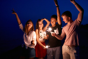 Friends walking, dancing and having fun during night party at the seaside with bengal sparkler...