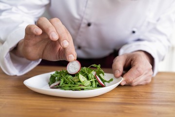 male cook chef decorating garnishing prepared salad dish on the plate in restaurant commercial kitchen.