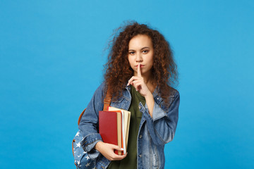 Young african american girl teen student in denim clothes, backpack hold books isolated on blue wall background studio portrait. Education in high school university college concept. Mock up copy space