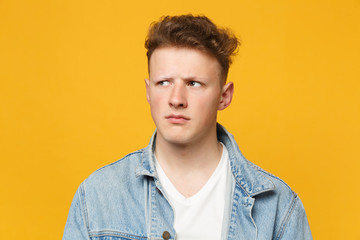 Portrait of preoccupied pensive young man wearing denim casual clothes looking aside isolated on yellow orange wall background in studio. People sincere emotions lifestyle concept. Mock up copy space.