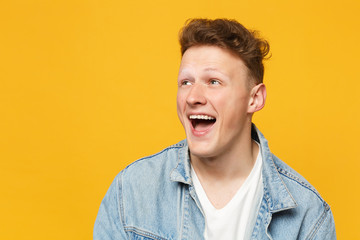 Obraz premium Portrait of laughing funny young man wearing denim casual clothes looking aside isolated on yellow orange wall background in studio. People sincere emotions, lifestyle concept. Mock up copy space.