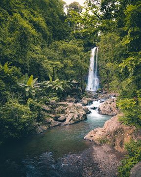 Woman standing in the distance in front of huge waterfall in Bali, Indonesia.