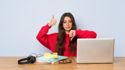 Teenager student girl studying in a table making good-bad sign. Undecided between yes or not