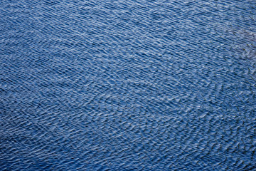 Blue lake water with ripples surface. Rippled water texture. Small waves in the pond. Fresh clean water texture. Selective focus. Copy space.