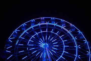 Glowing ferris wheel in an amusement park against a black night sky. Close-up