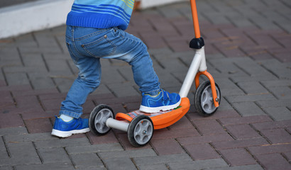 Boy child in blue jeans and sneakers riding a scooter. Legs closeup