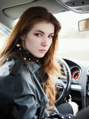 Fototapeta na wymiar Close up portrait of young attractive red hair self-employed business woman driver looking back from the driver's seat stuck in a city traffic jam noonday bleached colors cloudy weather