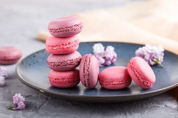 Purple and pink macaron or macaroon cakes on blue ceramic plate on gray concrete background.