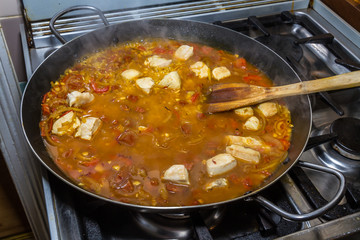Cooking chicken paella with wooden spatula on hob