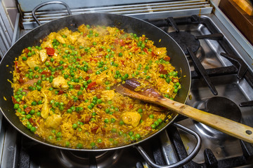 Cooking chicken paella with wooden spatula and green peas on hob