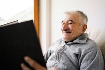 Senior old man watching looking a book family album photos at the retirement nursing home smiling - Powered by Adobe