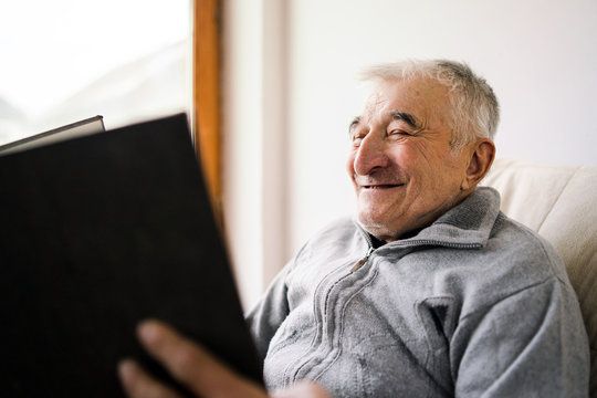 Senior old man watching looking a book family album photos at the retirement nursing home smiling