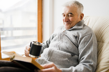 Senior man old sitting and Reading a book at the retirement nursing home with cup of tea in hand - obrazy, fototapety, plakaty