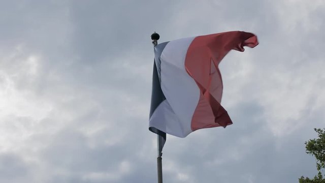 Flag of France waving on a flagpole in the wind against the blue sky. The concept of patriotism. Slow Motion.