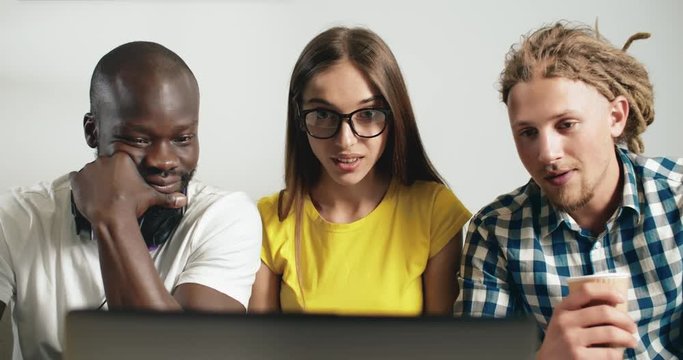 Three multirace casually dressed friends watching laptop with unexpectable shocked face expression