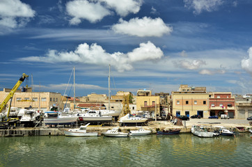 Fototapeta na wymiar Kleiner Hafen mit Booten und Häusern auf Sizilien vor blauem Himmel mit Wolken