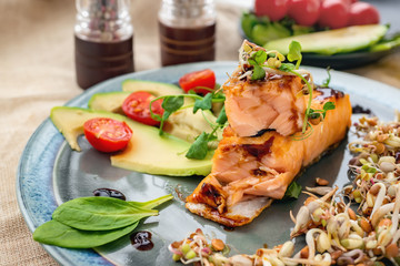 A piece of baked red fish with a side dish of sprouts and avocado salad. Macrobiotic food concept. Healthy food