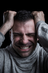 Studio portrait of a desperate man with hands on his head. Isolated on black background. Vertical.