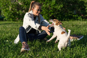 young white girl in a denim suit is training a pet dog jack russell terrier on the street