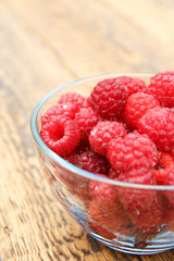 Ripe raspberries in the glass bowl on wooden boards.