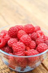 Ripe raspberries in the glass bowl on wooden boards.