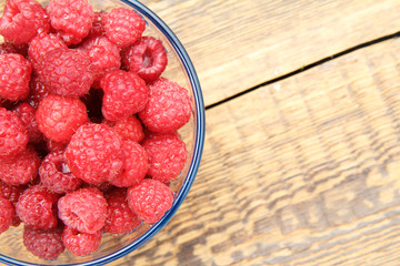 Ripe raspberries in the glass bowl on wooden boards.