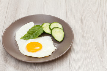 Plate with fried egg, fresh cut cucumber and leaf of basil.