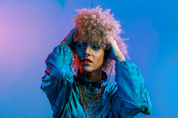 Young beautiful woman with big blond afro hair in colorful studio shoot, wearing gold chains and 