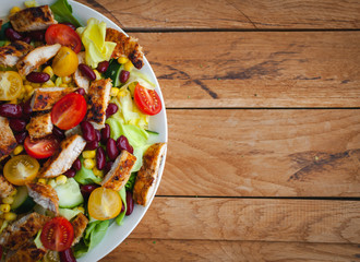Close-up of chicken salad with fresh vegetables in a plate, on wooden background, top view