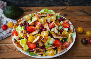 Close-up of chicken salad with fresh vegetables in a plate, on wooden background