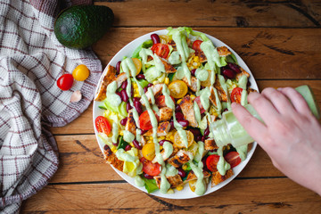 Close-up of chicken salad with fresh vegetables in a plate and avocado dressing, on wooden background, top view