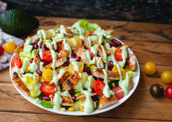 Close-up of chicken salad with fresh vegetables in a plate and avocado dressing, on wooden background