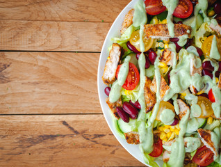 Close-up of chicken salad with fresh vegetables in a plate and avocado dressing, on wooden background, top view