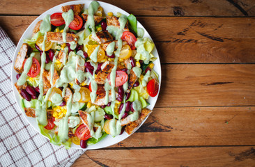 Close-up of chicken salad with fresh vegetables in a plate and avocado dressing, on wooden background, top view