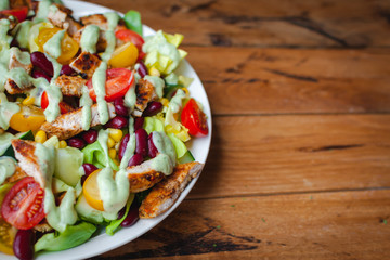 Close-up of chicken salad with fresh vegetables in a plate and avocado dressing, on wooden background