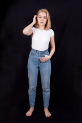 Young woman in white t-shirt and blue jeans is standing on a black background