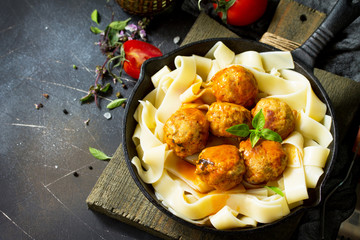 Fettuccine pasta and Homemade Beef meatballs in tomato sauce in a frying pan on dark stone table. Free space for your text.