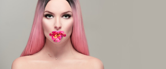 Beauty model girl with pink flower in her mouth. Beautiful spring young romantic woman with pink hair posing with Alstroemeria flower on her lips over gray background