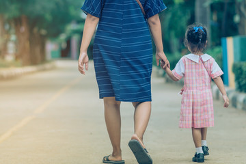 Mom and daughter pupil girl holding hand in hand on street go to the classroom together.