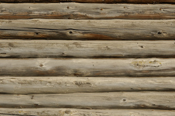 The wall of the house, made of planed pine logs. The logs are old, visible cracks and burnt areas.