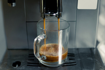Cup in the coffee machine. The process of making coffee. Coffee slowly flows into the cup