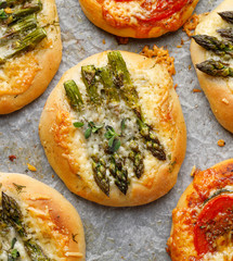 Small pizzas with the addition of green asparagus, tomatoes, cheese and herbs, top view, close-up. Vegetarian pizzas, delicious appetizer