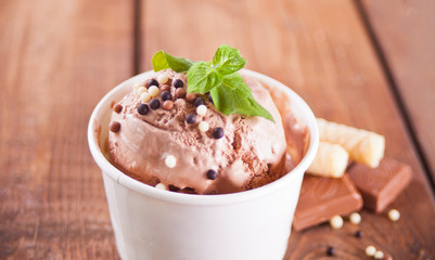 Paper bowl of chocolate ice cream, waffle cone and spoon for ice cream on wooden background.