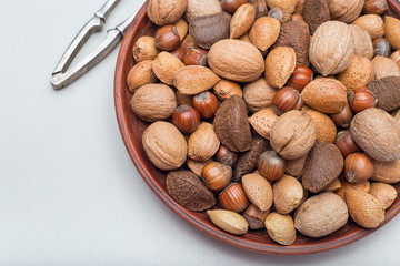 Different kinds of nuts in the shell, hazelnut, walnut, almond and brazil nuts on  ceramic plate with nut cracker on background, horizontal, copy space, top view