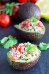 Salad with tuna, avocado, tomatos, coriander and lemon juice served in avocado bowls, ingredients on background, vertical