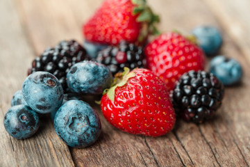 Fresh Summer Berries mix with Strawberry, Raspberry, Red currant, Blueberry and Blackberry on wood background.